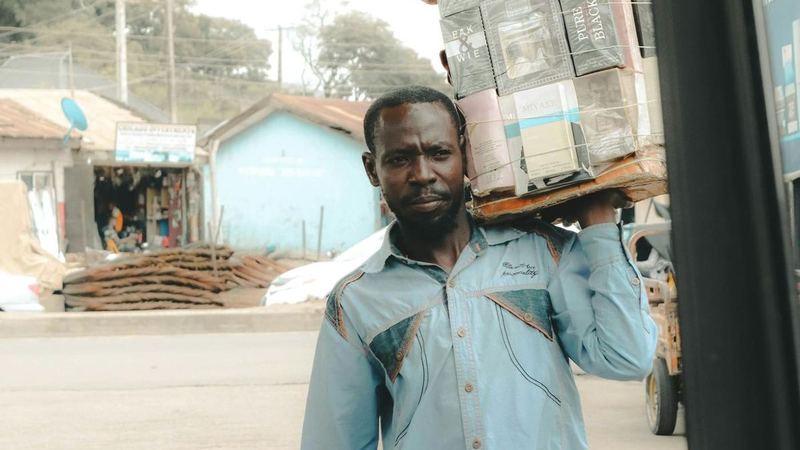 A man carrying a stack of cartons on his shoulder beside the open door of a vehicle