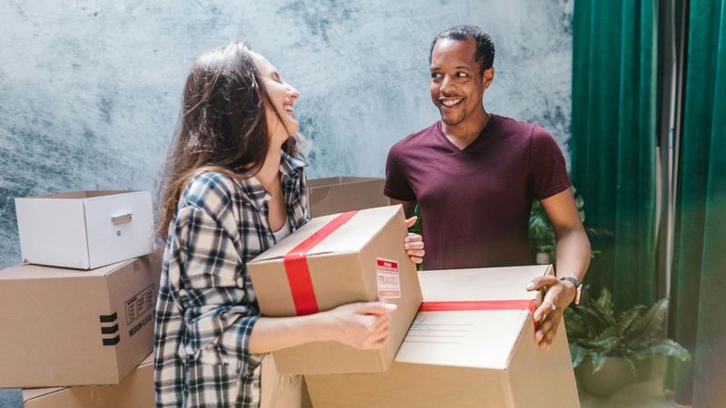 Two people carrying cardboard boxes together during a home move